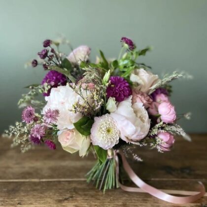A lush dahlia and peony bouquet featuring soft pink peonies and vibrant white dahlias with green foliage.