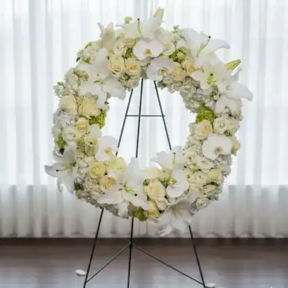 An elegant funeral wreath on stand featuring white orchids and lilies, symbolizing a peaceful and respectful tribute.