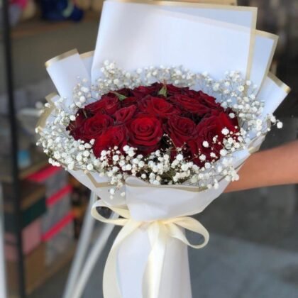 A hand-tied luxury bouquet of 18 red rose blossoms with lush green leaves in a premium wrap.