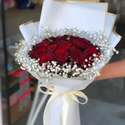 A hand-tied luxury bouquet of 18 red rose blossoms with lush green leaves in a premium wrap.