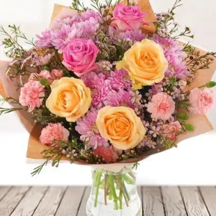 A beautifully arranged chrysanthemum and roses bouquet featuring soft pink petals and lush green foliage in a natural setting.