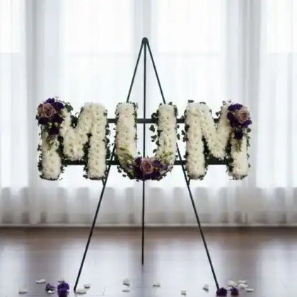 A beautiful floral arrangement forming mum funeral letters using white carnations with pink and purple rose accents.