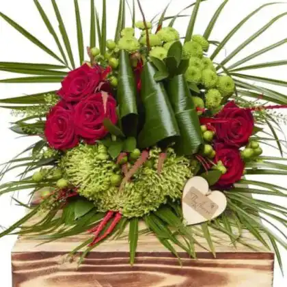 A hand-tied rose and hypericum bouquet featuring deep red petals and textured green berries in a glass vase.
