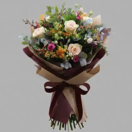 Hand-tied snapdragon and rose bouquet featuring peach roses and magenta spray roses in rustic kraft paper wrap.