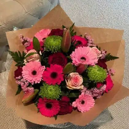 Hand-tied gerbera daisy bridal bouquet featuring soft pink petals and fresh green foliage for a spring wedding.
