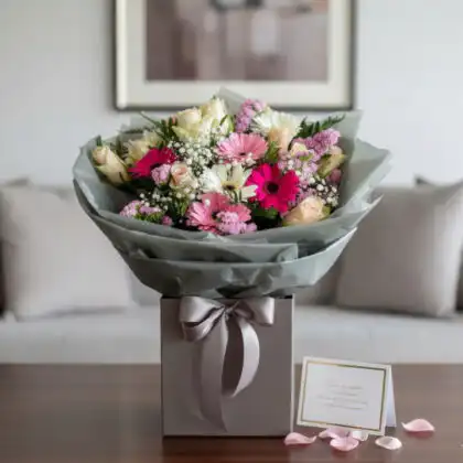 A hand-tied light pink gerbera daisy bouquet accented with soft cream roses and fresh green foliage.