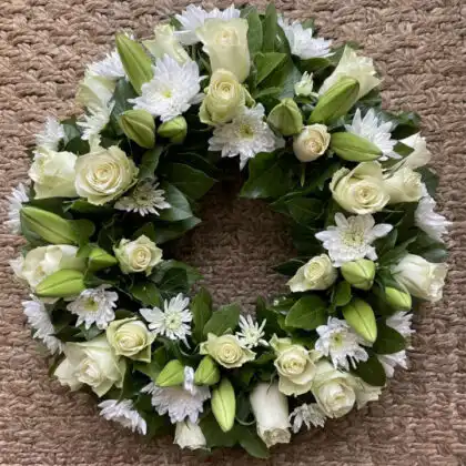 A serene white rose and lily wreath arranged with lush greenery, ideal for memorial tributes and elegant ceremonies.