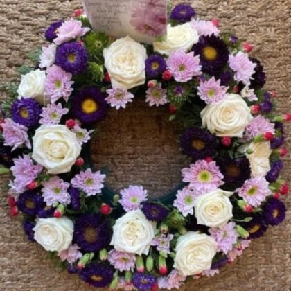 A beautiful Purple and White Funeral Wreath composed of fresh cream roses and vibrant violet blossoms.