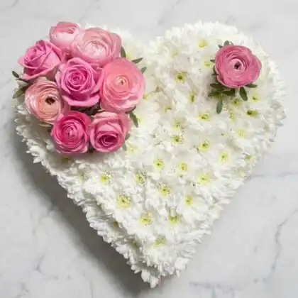 A funeral flower heart arrangement featuring delicate pink roses and white lilies as a peaceful memorial tribute.