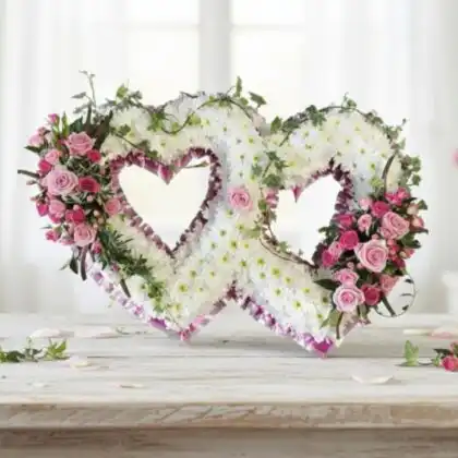 A pair of interlocking funeral flowers double heart wreaths crafted with fresh white and pink roses for a memorial service.