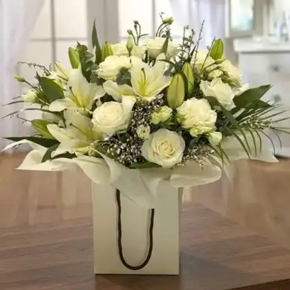 Hand-tied flower bouquet lily and rose with white blooms and fresh eucalyptus leaves in a cream gift bag.