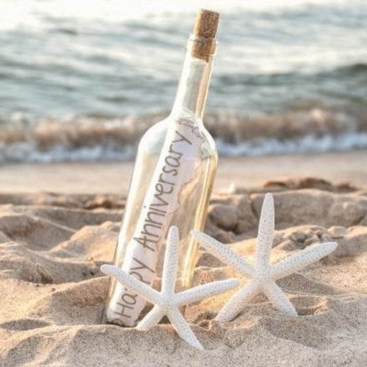 Happy Marriage Anniversary Greeting Cards 1 A Marriage Anniversary Greeting Card rolled inside a glass bottle on a sandy beach with two white starfishes.