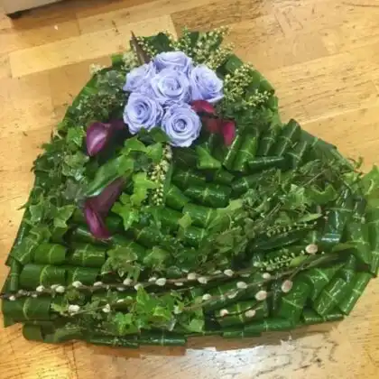 Handcrafted Large Heart Funeral Tribute featuring lavender roses and deep purple calla lilies on a green leaf base.