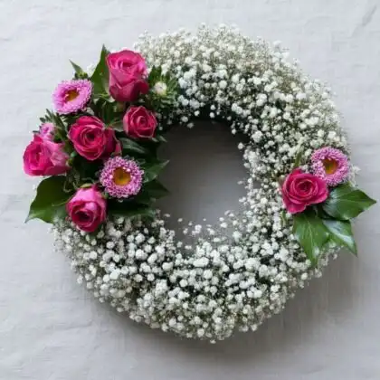 A sympathy arrangement of elegant pink rose and aster floral wreaths for funeral services, displayed on a wooden stand.