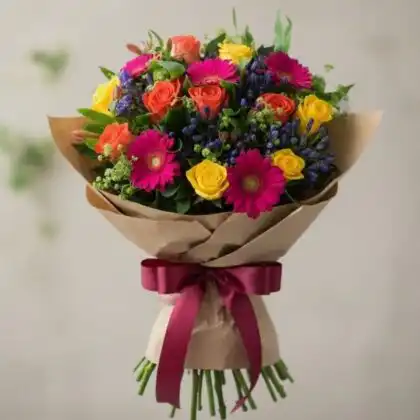 A hand-tied rose and gerbera daisy bouquet featuring bright yellow roses and soft pink petals in a decorative wrap.