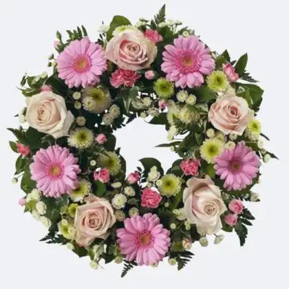 A circular Pink and Cream Funeral Wreath composed of fresh roses, gerberas, and green foliage against a white background.