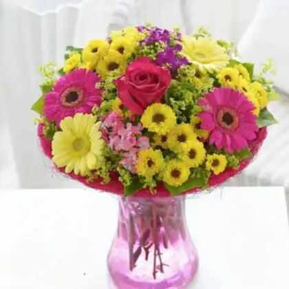 Hand-tied yellow and pink gerberas bouquet arranged with fresh greenery in a bright studio setting.