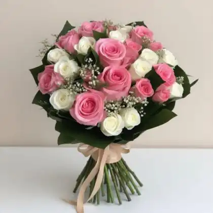 A handcrafted bouquet of white and pink roses tied with a satin ribbon, showcasing fresh blooms and green foliage.