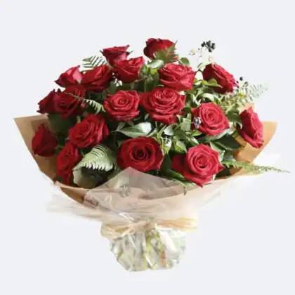 A vibrant hand-tied red rose bouquet wrapped in rustic kraft paper with fresh green leaves and berries.