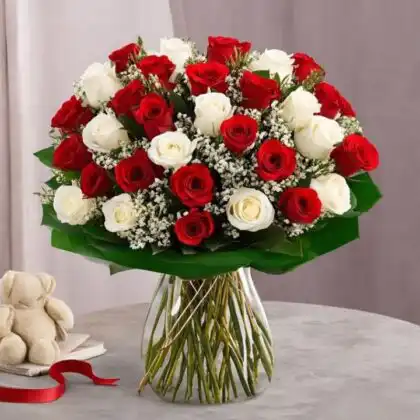A fresh white and red roses bouquet arranged with baby's breath in a clear glass vase on a wooden table.