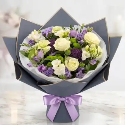 A hand-tied white rose and carnation bouquet accented with lush green foliage in a minimalist setting.