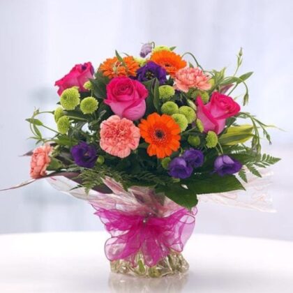 Rose and Gerbera Daisy Bouquet featuring bright pink roses, striking orange Gerbera daisies, peach carnations, and deep purple accent flowers, beautifully wrapped with a sheer pink ribbon.