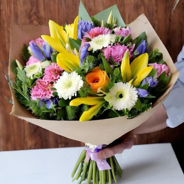 Mother's Day Spring flowers Hand tied Bouquet UK held in a man's hand with vibrant roses, tulips, and lilies.