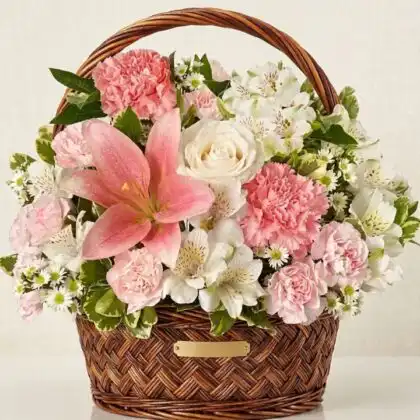 A handcrafted basket flower arrangements featuring white lilies, pink roses, and carnations in a woven wicker base.