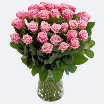 Handcrafted bouquet of fresh pink roses arranged in a clear glass vase with green leaves.