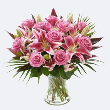 A fresh Pink roses Bouquet with stargazer lilies and green palm leaves in a clear glass vase.