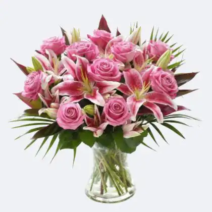 A fresh Pink roses Bouquet with stargazer lilies and green palm leaves in a clear glass vase.