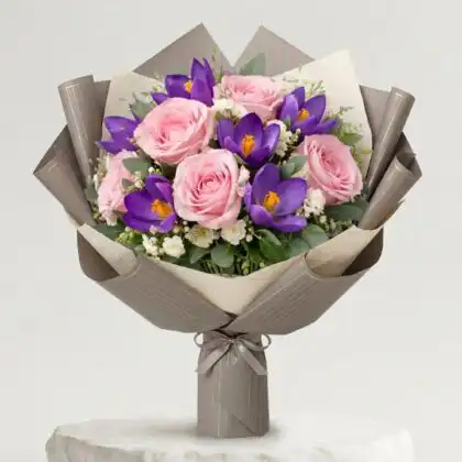 A hand-tied bouquet featuring a vibrant purple crocus flower nestled among soft roses and seasonal greenery.