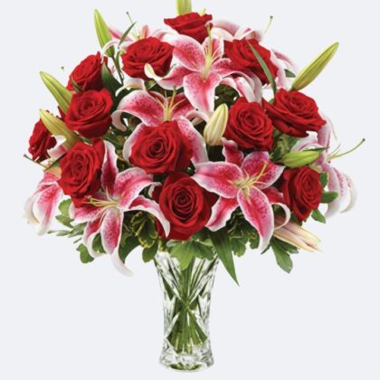 A luxury glass vase holding fresh bouquets with lilies and roses in vibrant red and pink shades.