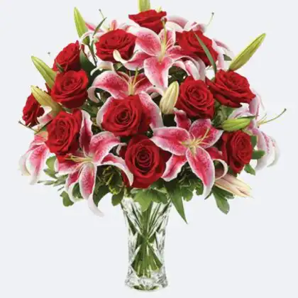 A luxury glass vase holding fresh bouquets with lilies and roses in vibrant red and pink shades.