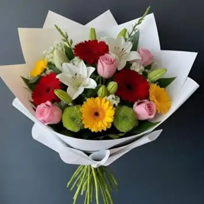 A vibrant rose and gerbera bridal bouquet featuring pink roses, red gerberas, and white lilies wrapped in white paper.
