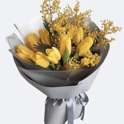 A stunning Yellow Tulips Bouquet accented with golden mimosa and elegant silver gift wrapping.