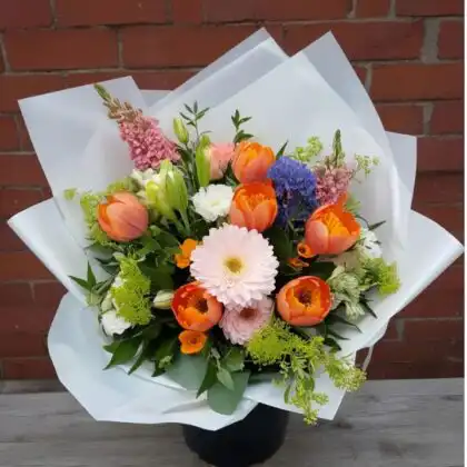 Hand-tied Gerbera and Tulip Bouquets featuring bright orange tulips and soft pink gerberas in white wrap.