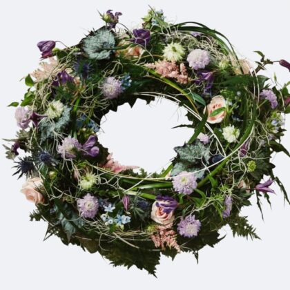 A beautiful arrangement of Natural Funeral Wreaths featuring seasonal pink roses and purple wildflowers designed for a respectful memorial tribute.