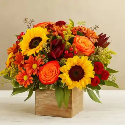 A stunning floral autumn box arrangement featuring deep red, orange, and yellow seasonal flowers with pine cones in a rustic wooden box.