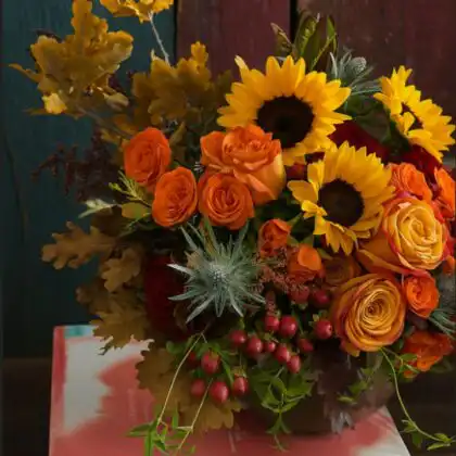 Vibrant Autumn hand tied floral bouquet with sunflowers, orange roses, red hypericum berries, and fall leaves.