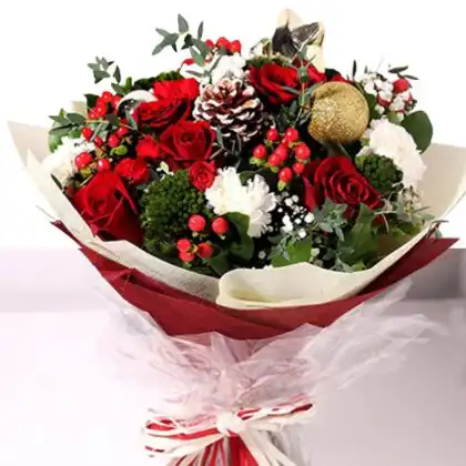 Festive hand-tied bouquet featuring red roses, white carnations, red berries, pine cones, and a glittery gold bauble, wrapped in red and white festive paper. Buy Red Christmas Flower Bouquet Delivery next day