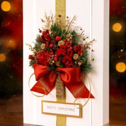 A luxurious white Christmas gift card decorated with a red floral/pine tree design, gold ribbon, and a large red satin bow.
