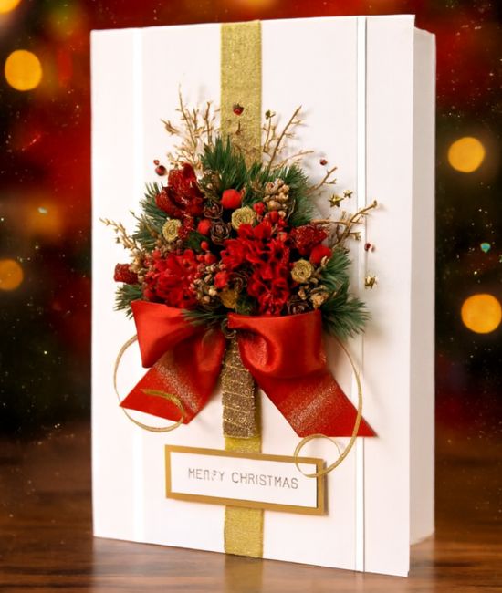 Blog 11 A luxurious white Christmas gift card decorated with a red floral/pine tree design, gold ribbon, and a large red satin bow.