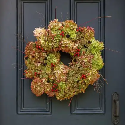 A beautifully natural luxury Christmas wreath for a front door, made from dried hydrangea flowers, red berries, and delicate twigs, hanging on a dark gray door. Luxury Christmas Wreaths For Front Door for sales