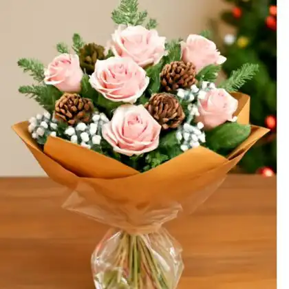 Hand-tied pink Christmas bouquet with fresh pink roses, snowy accents, natural pine cones, and pine foliage, wrapped in a brown paper cone.