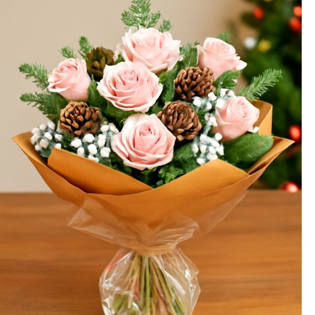 Blog 13 Hand-tied pink Christmas bouquet with fresh pink roses, snowy accents, natural pine cones, and pine foliage, wrapped in a brown paper cone.