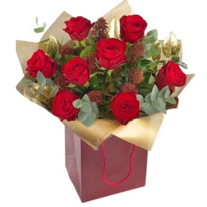 Vibrant red rose Christmas fresh flower arrangement with golden foliage and dried accents, beautifully packaged in a festive red gift bag. Christmas fresh flower arrangements For sale