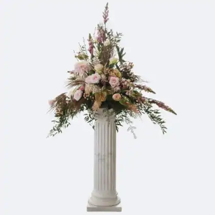 A large and elegant pedestal flower arrangement featuring soft pink roses and lush greenery on a white marble column.