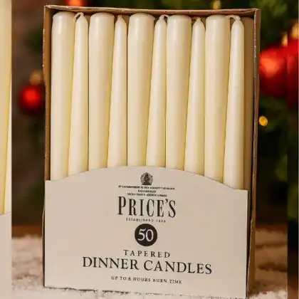 A box of elegant, cream-colored white tapered dinner candles by Price's, shown against a festive red Christmas background.