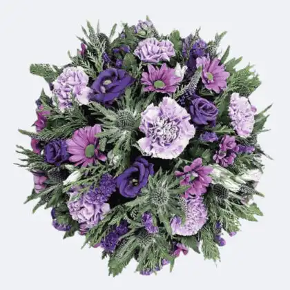 A round posy of flowers for a funeral featuring purple carnations, lisianthus, and blue thistle with green cedar foliage.